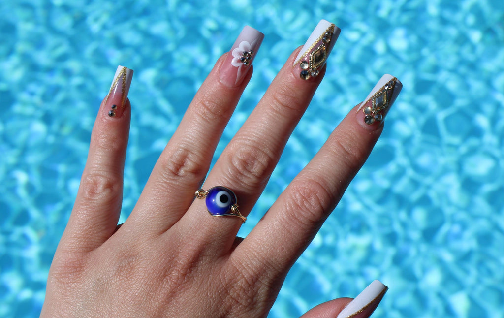 Hand with decorated nails and a blue evil eye ring against a pool background