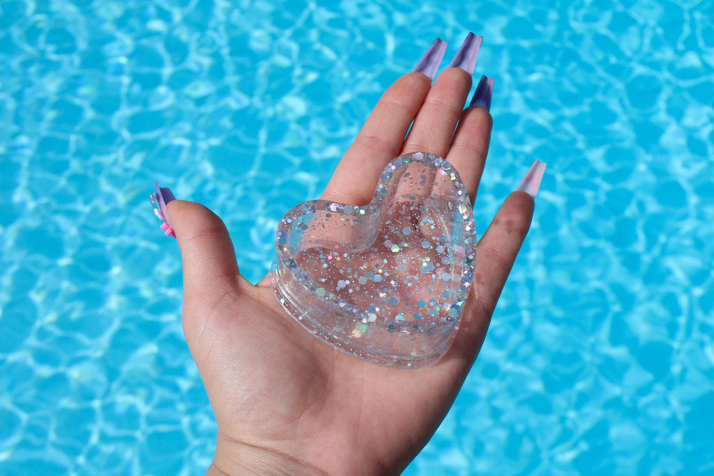 Heart-shaped glittery ring dish held in a hand with a blue water background