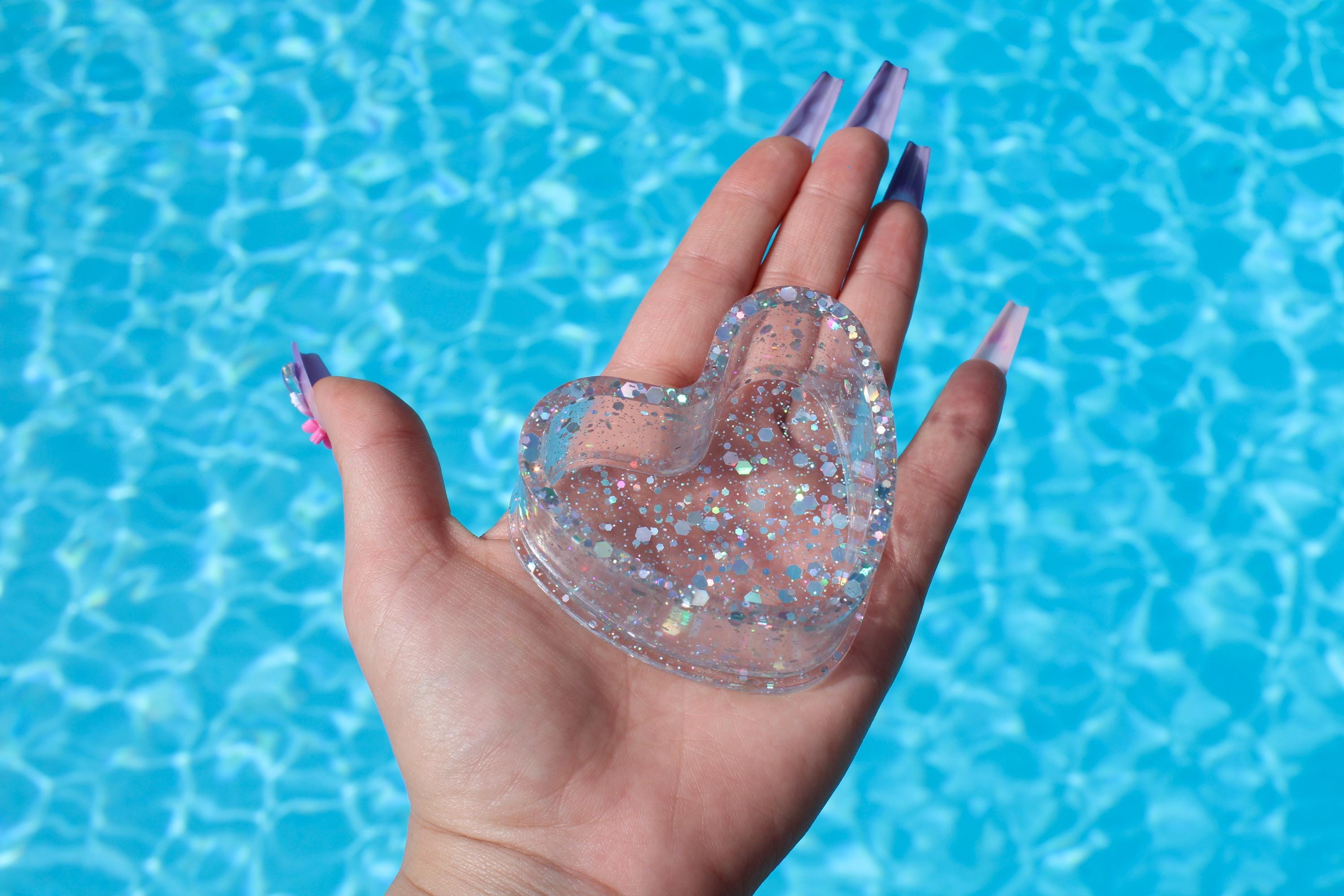 Heart-shaped glittery ring dish held in a hand with a blue water background