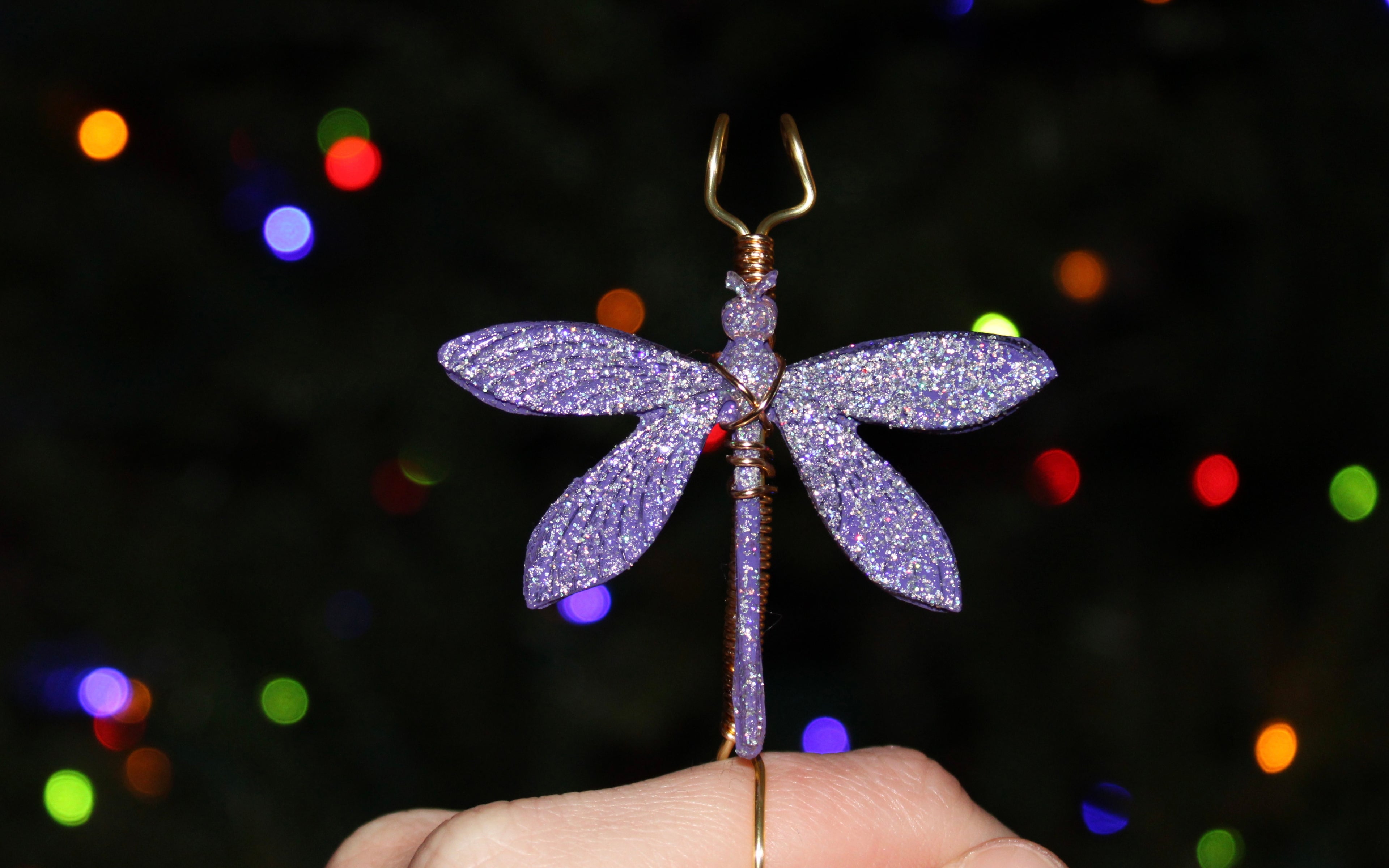 A hand holds a glittery purple dragonfly smoke ring against a backdrop of colorful lights.