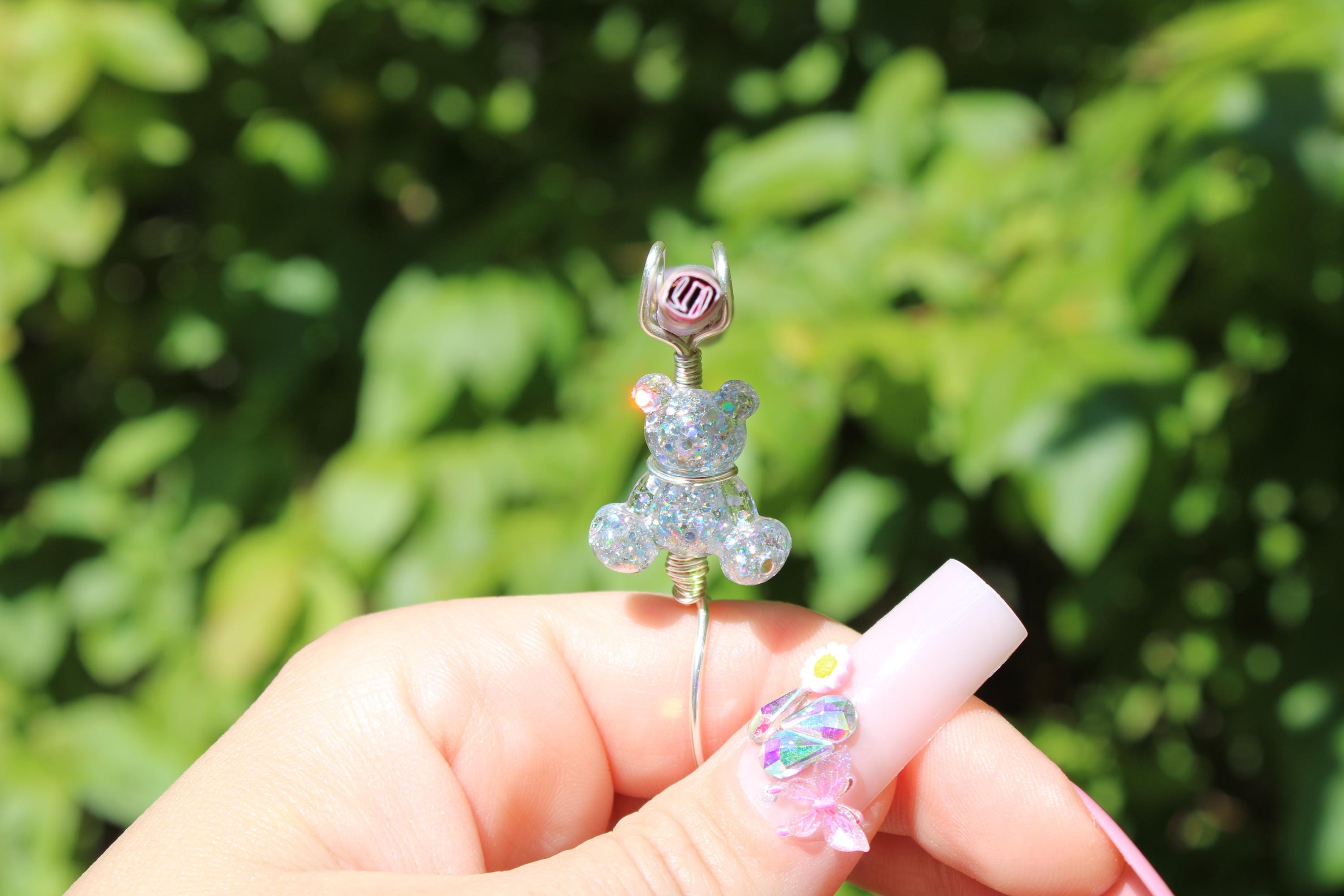 A manicured hand displays a silver sequin teddy bear wire wrapped as a ring used as a smoking accessory.