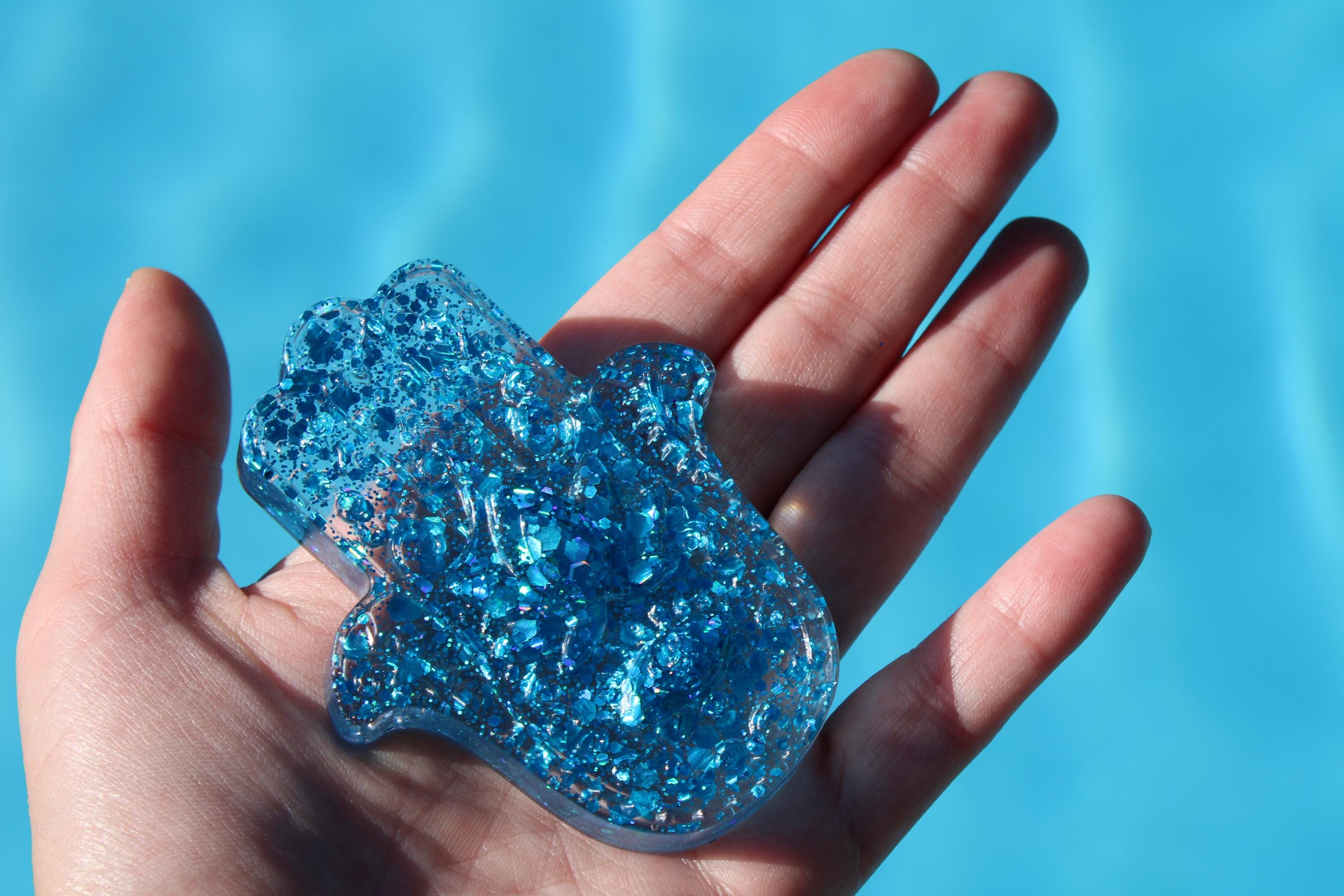 Hand holding a blue glittery hamsa hand against a blue background