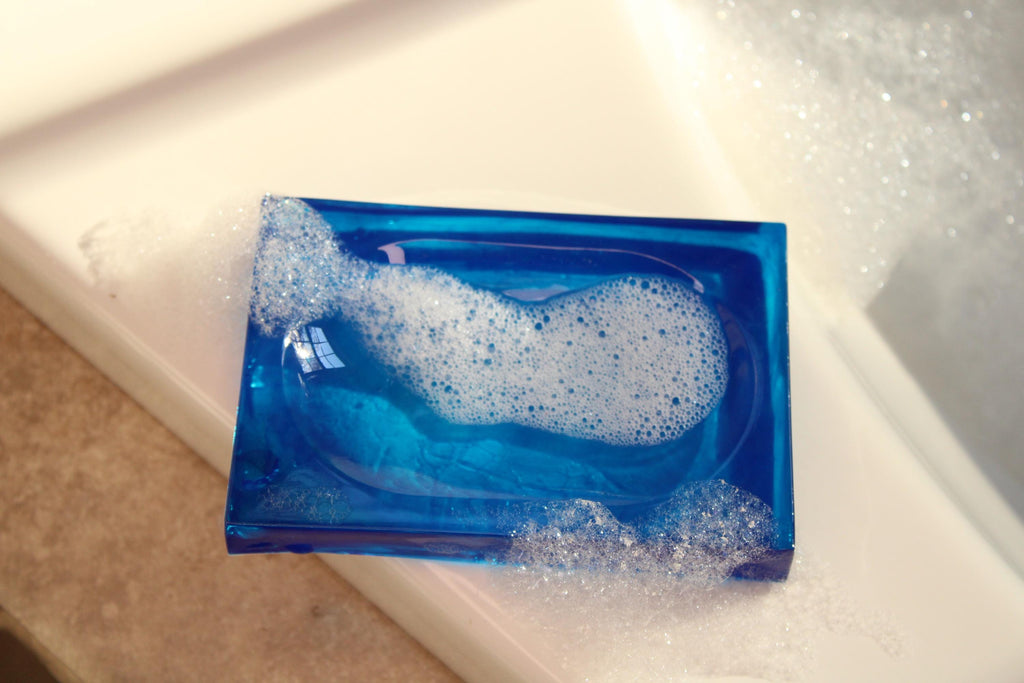 Blue soap dish holds bubbly, white lathering soap on a clean white surface.