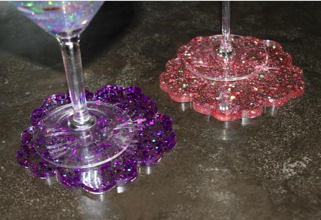 Two glittery resin drink coasters, one purple and one pink, on a dark surface.