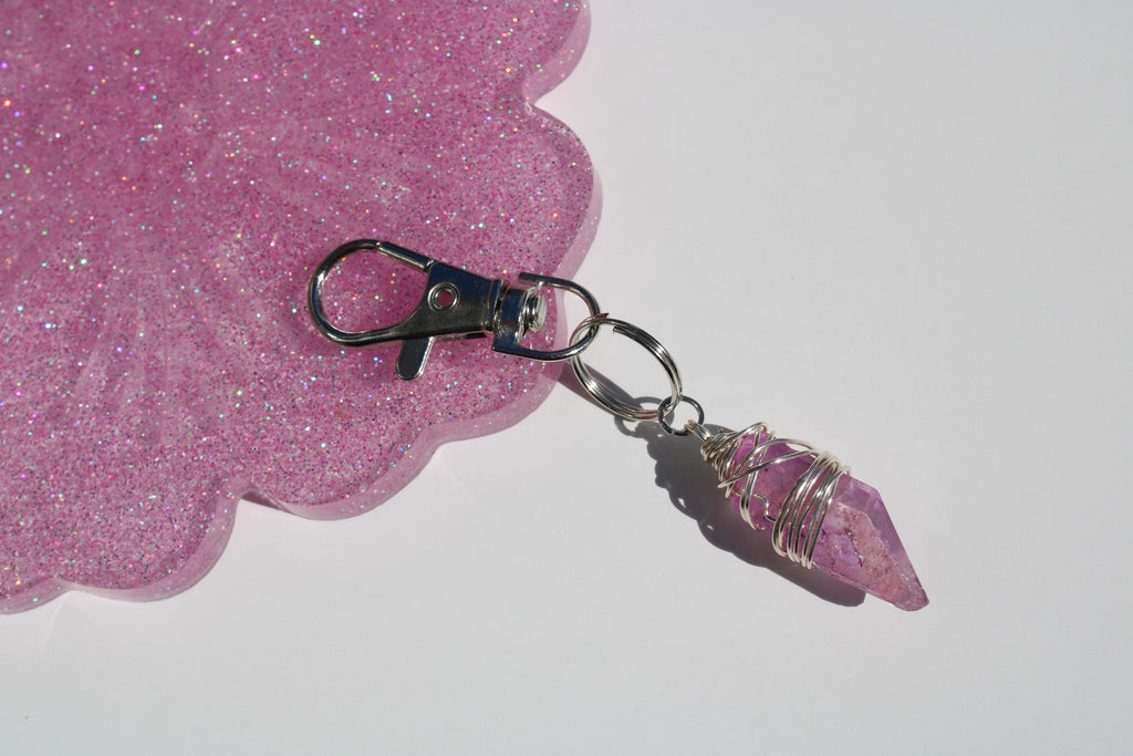 A wire wrapped rose quartz crystal pendant lies on white surface.