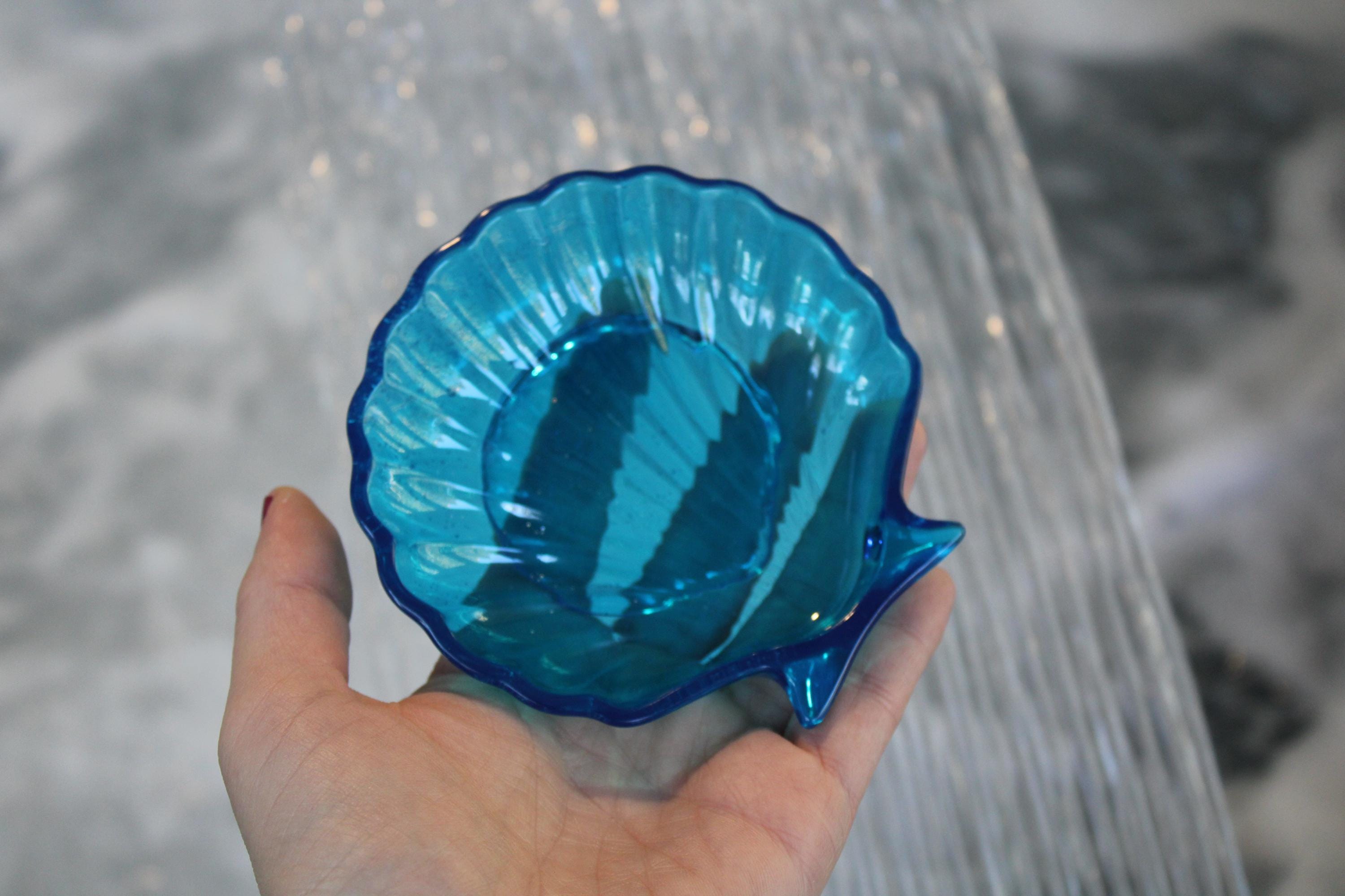 Hand holding a blue resin shell-shaped dish against a blurred background