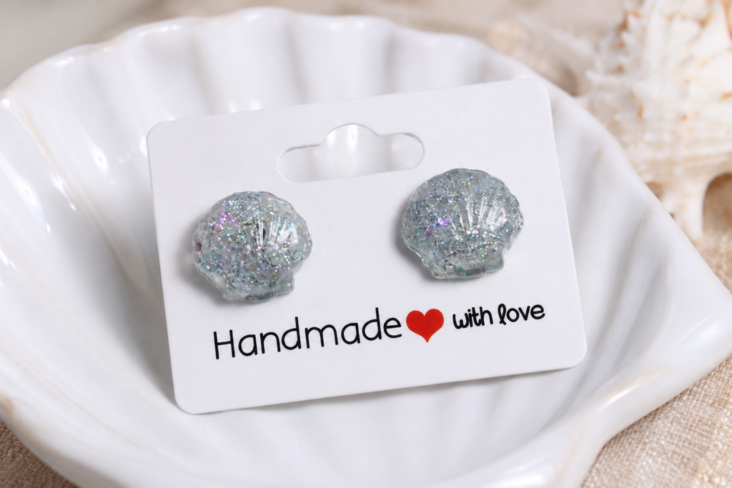 Silver glittery shell-shaped earrings on a 'Handmade with Love' card inside a white shell.
