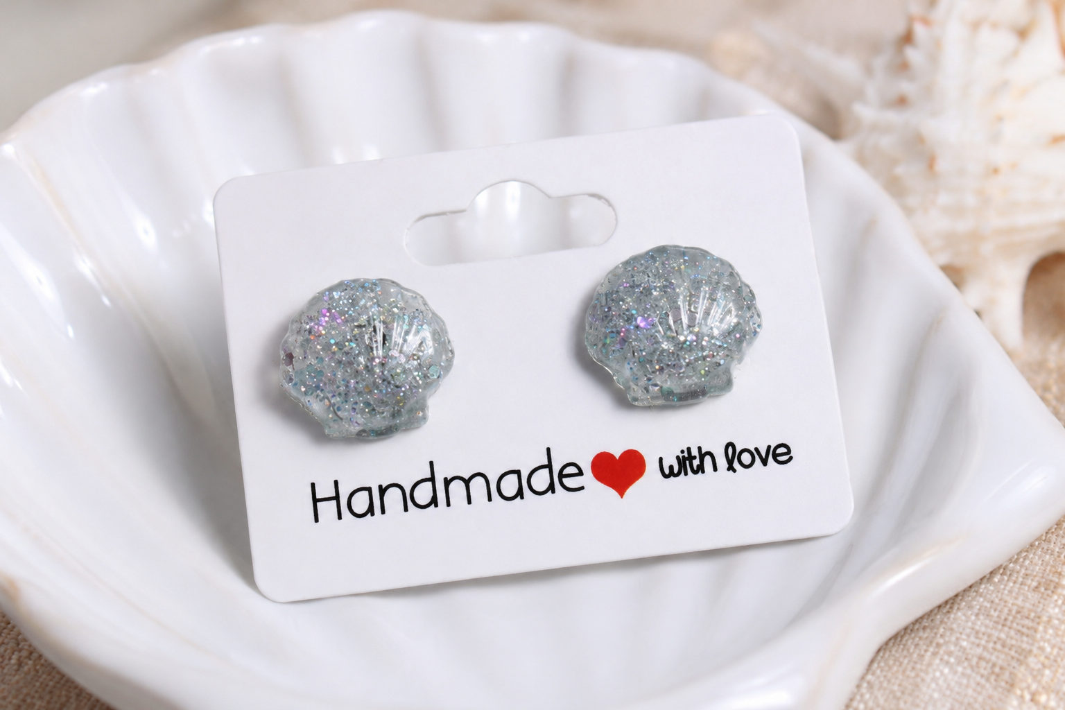 Silver glittery shell-shaped earrings on a 'Handmade with Love' card inside a white shell.
