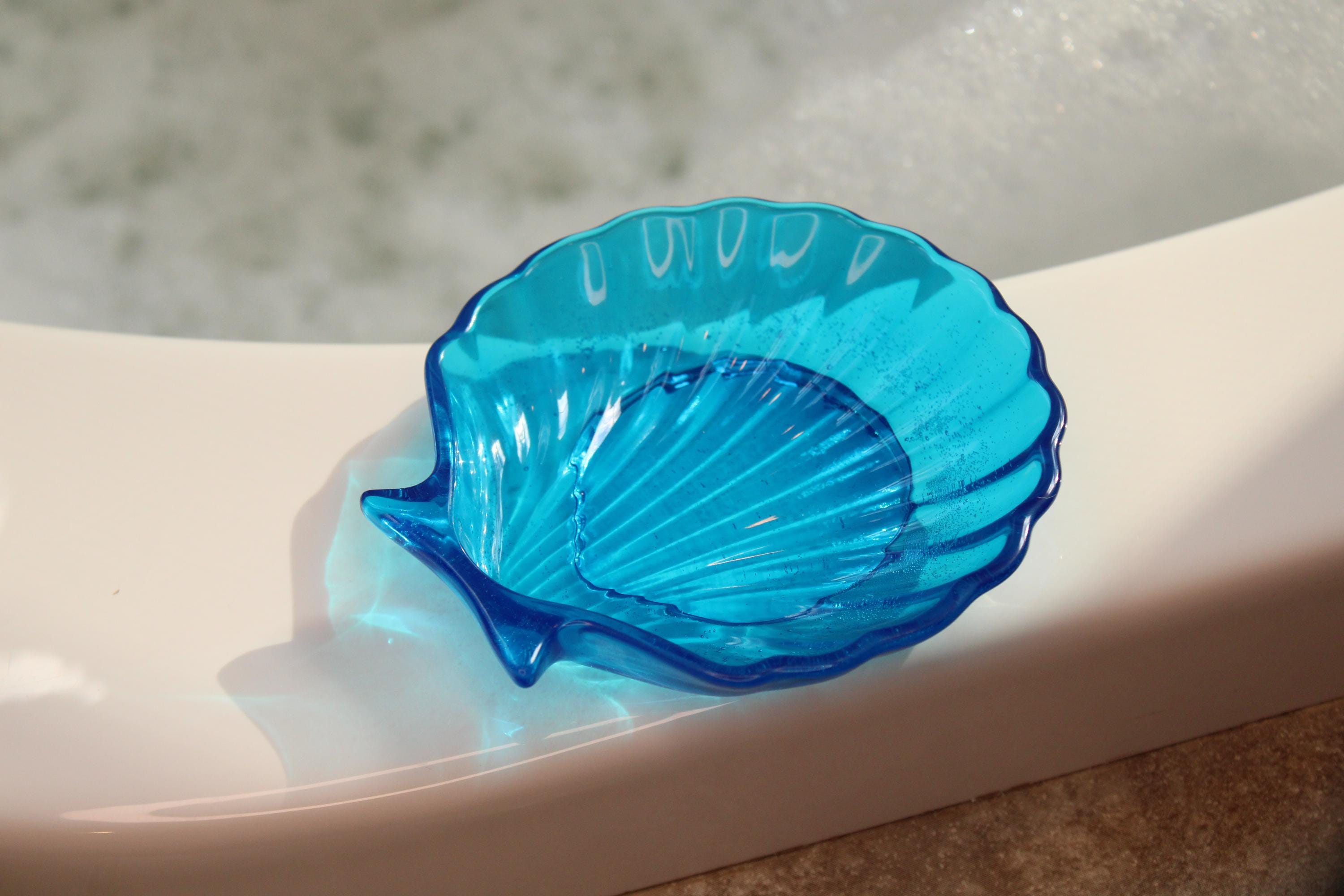 Blue shell-shaped object on a bathtub ledge with water in the background