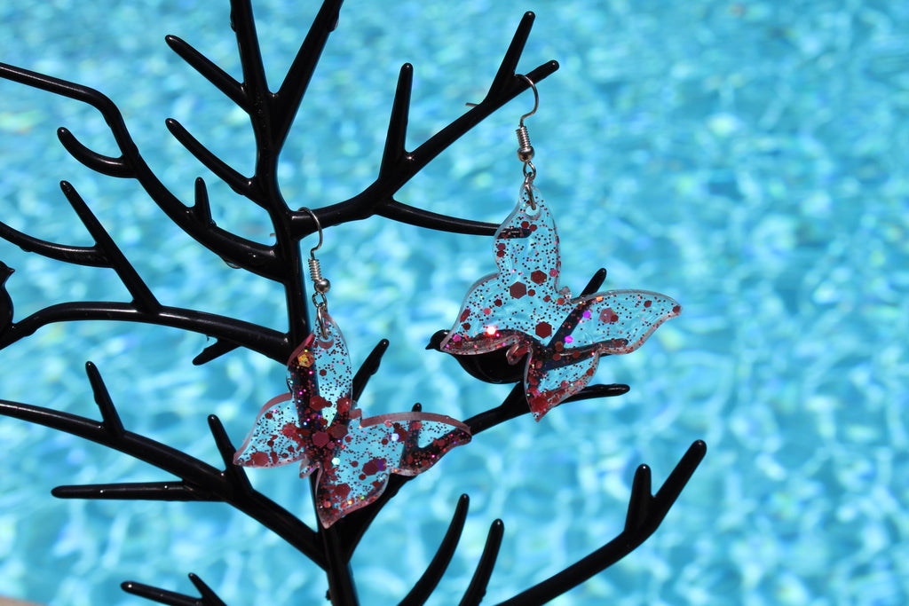 Butterfly-shaped earrings on a black branch against a blue water background
