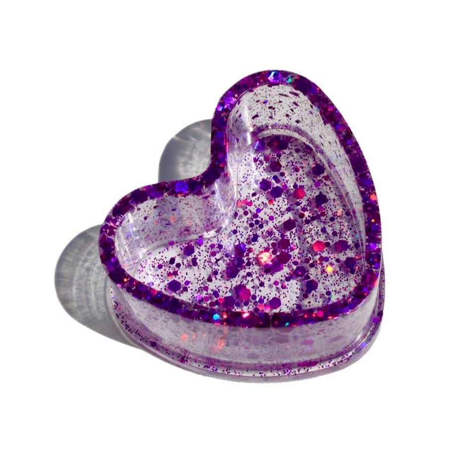 Heart-shaped ring dish with purple glitter on a white background