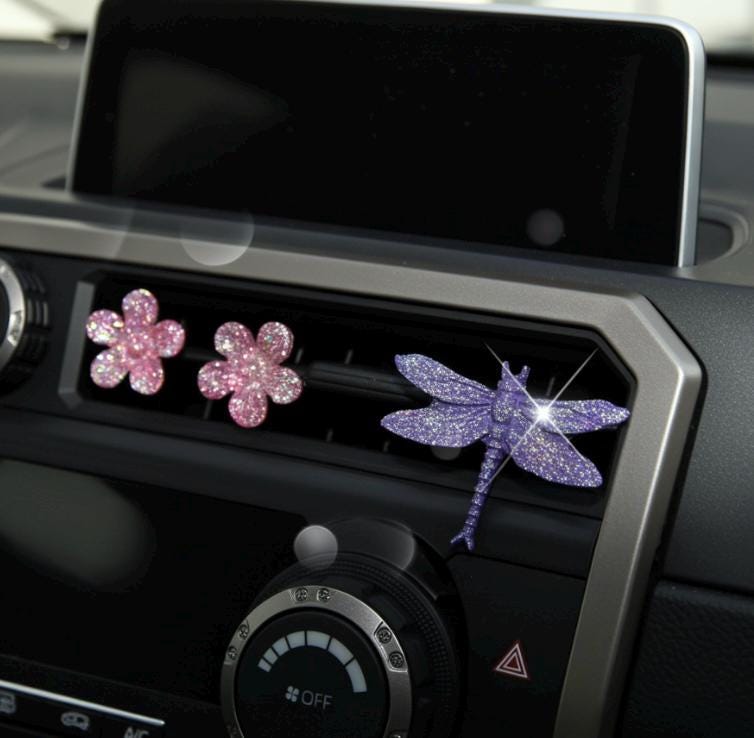 Decorative car vent clip with pink flowers and a purple dragonfly on a car dashboard.