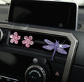 Decorative car vent clip with pink flowers and a purple dragonfly on a car dashboard.