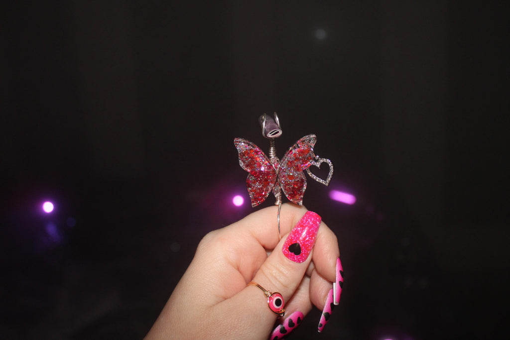 Butterfly-shaped smoke ring with red embellishments held by a hand against a dark background.