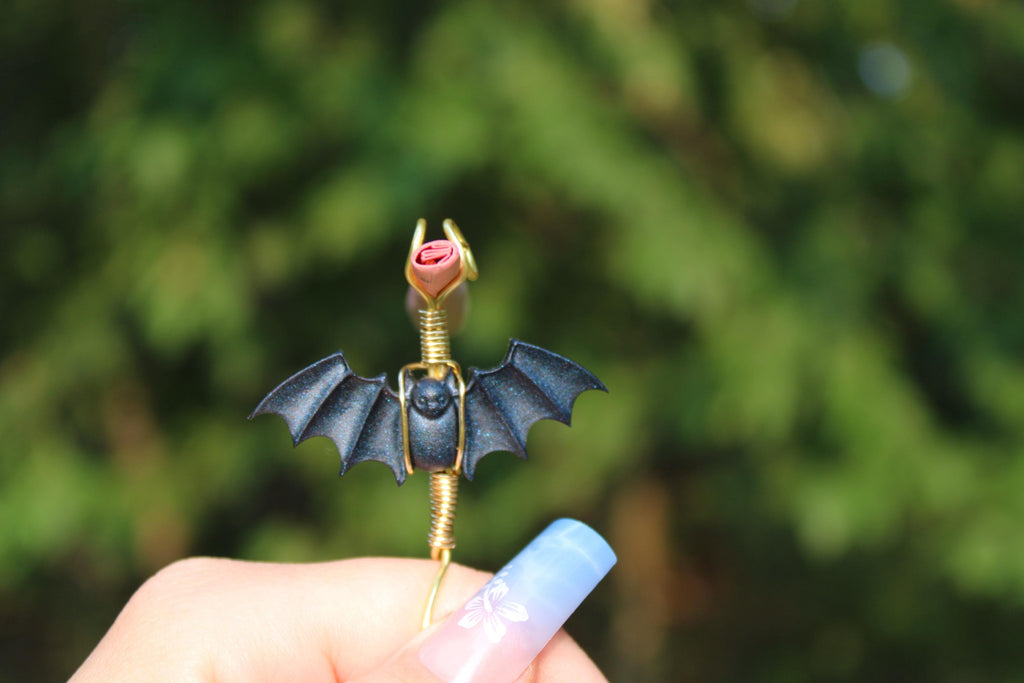 Hand displays a handmade gothic bat smoke ring in front of a leafy background.