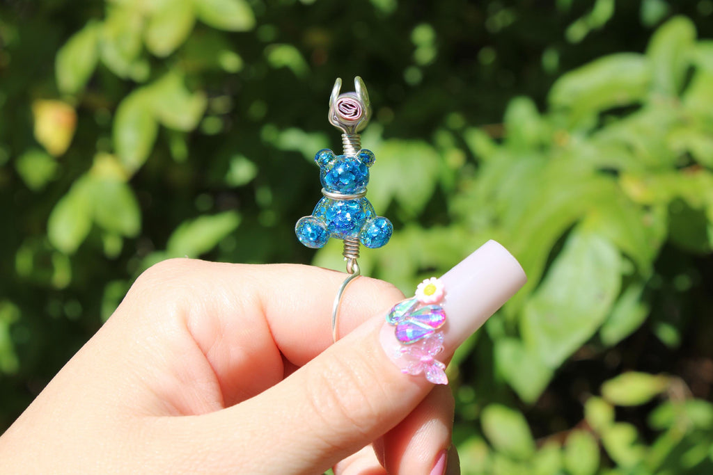 Hand holding a smoke ring with a blue bear design against a green leafy background