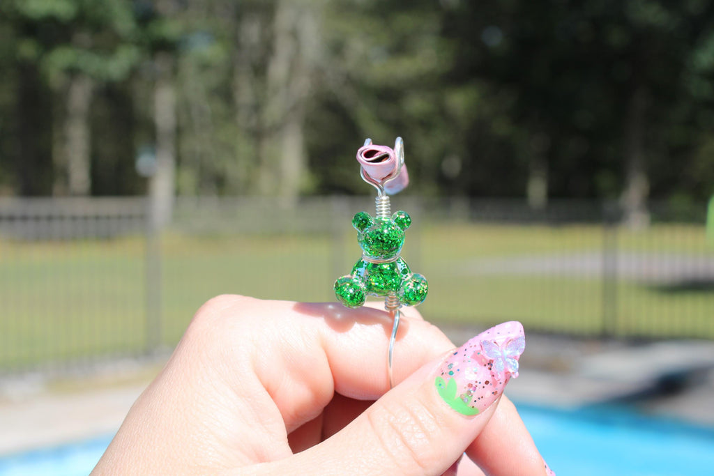 Hand displays a whimsical handmade smoke ring featuring a glittery green teddy bear.