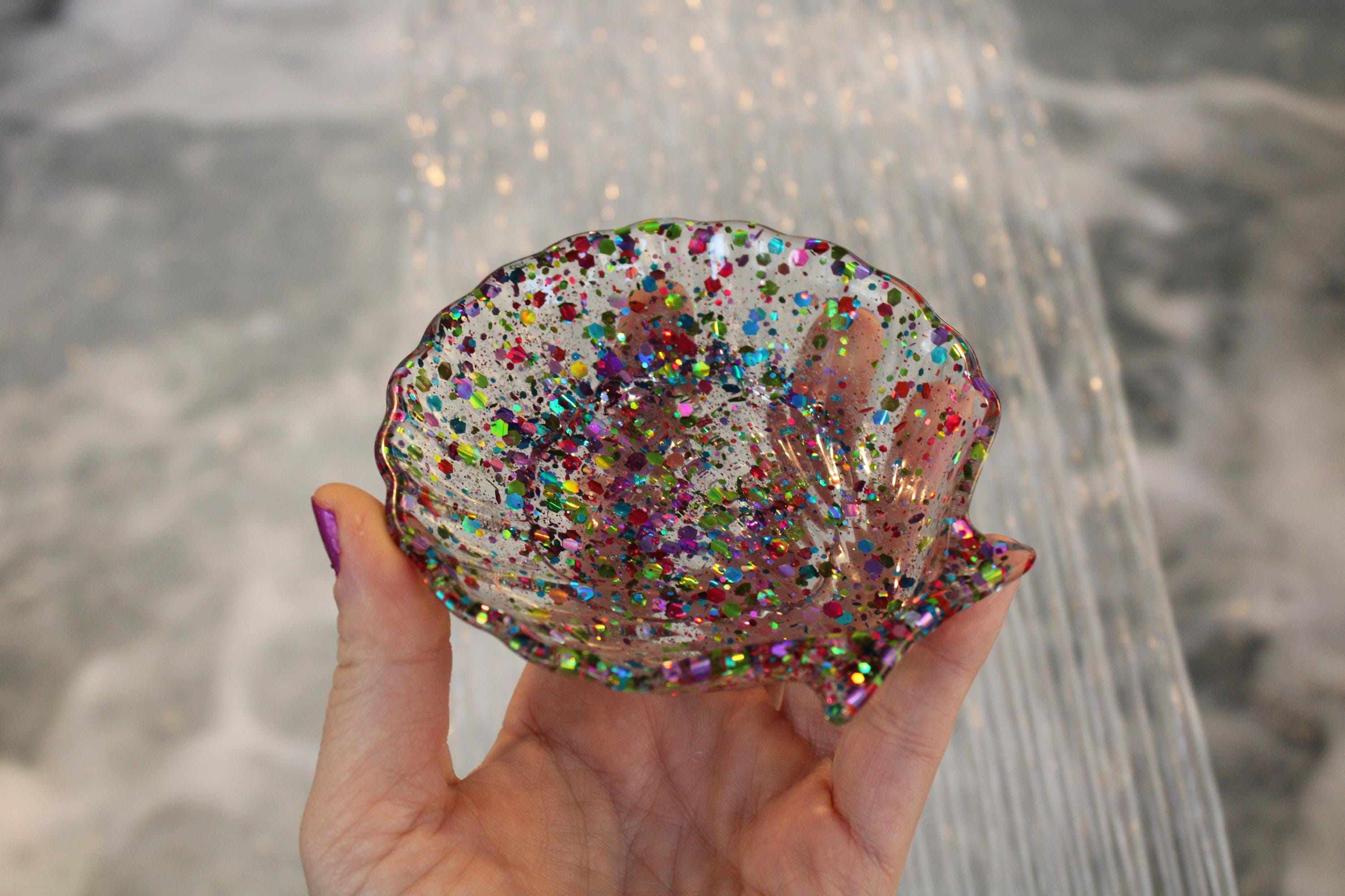 Hand holding a glittery shell against a blurred water background
