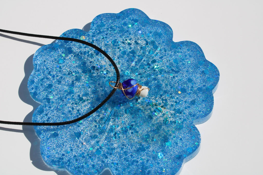 A blue pendant necklace rests on a sparkly, blue resin coaster.
