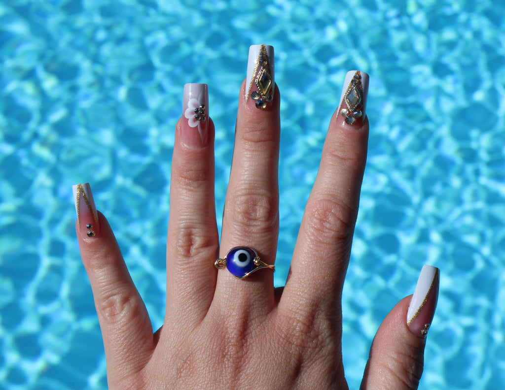 Hand with decorated nails and an evil eye ring against a blue water background