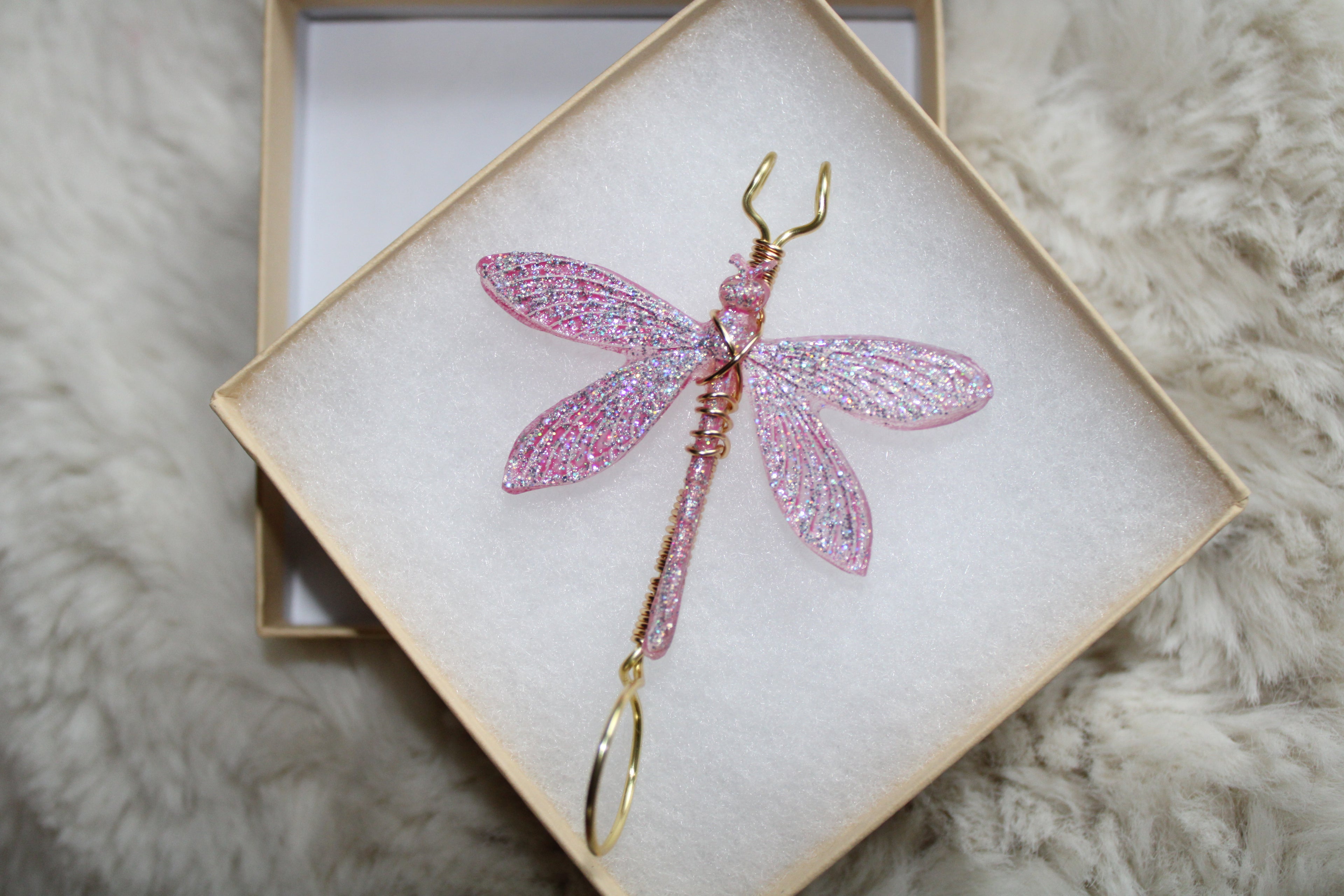 A handcrafted pink glitter dragonfly smoke ring rests in a gift box.