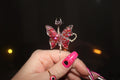 Butterfly-shaped smoke ring with pink gemstones held by a hand against a dark background