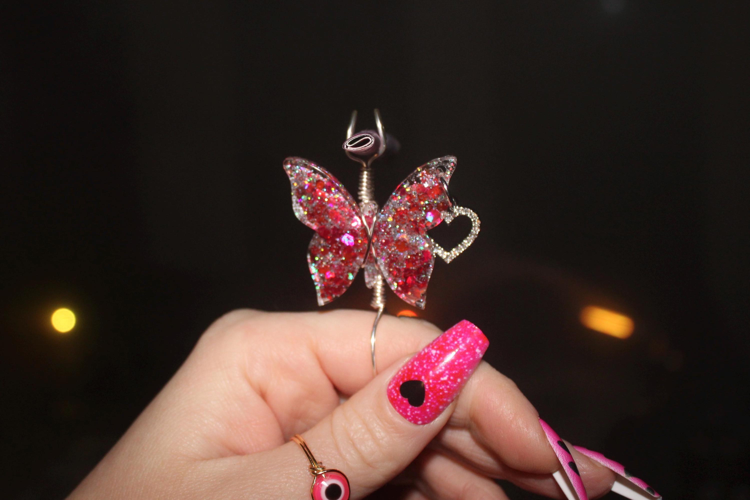 Butterfly-shaped smoke ring with pink gemstones held by a hand against a dark background