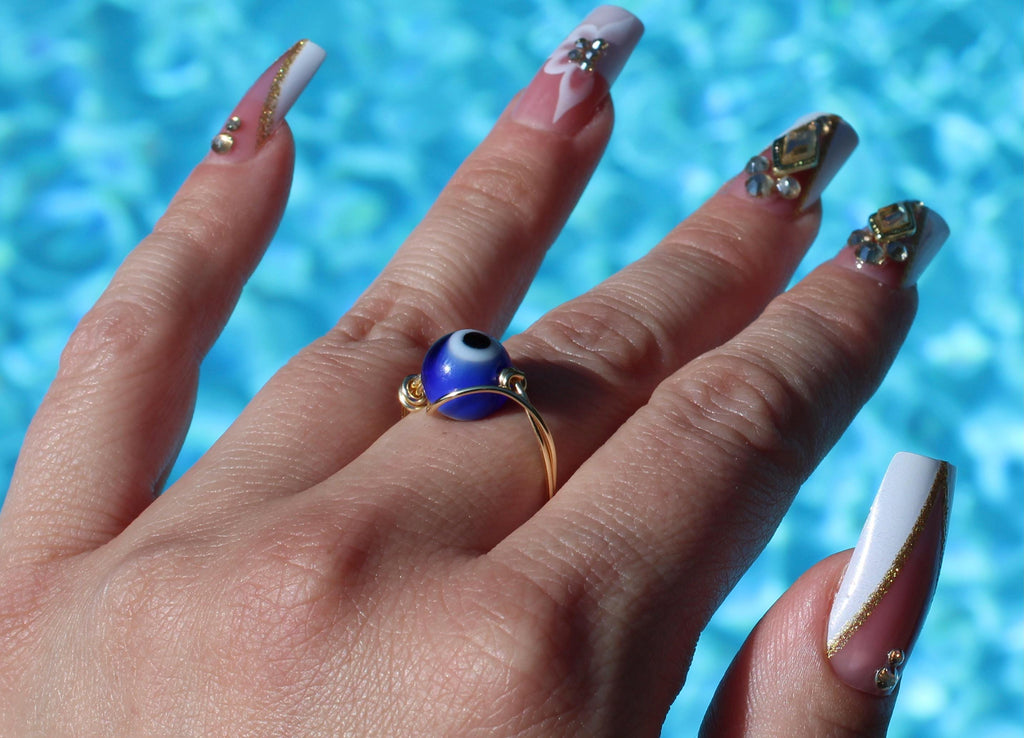 Hand wearing a blue evil eye ring against a blurred pool background