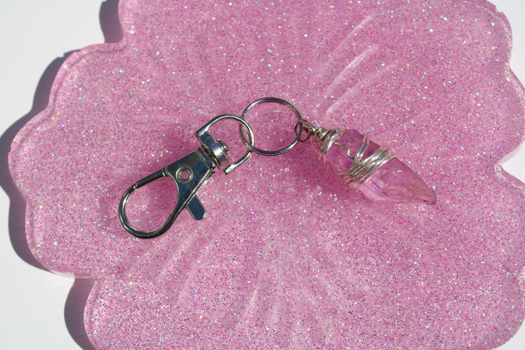 Rose quartz crystal keychain rests on a shimmering resin coaster.