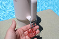 A hand displays a sparkling red weed leaf keychain attached to a Stanley cup near a pool.
