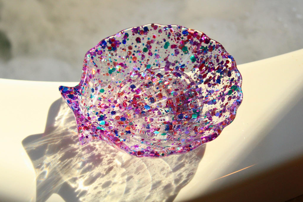 Colorful glittery shell-shaped dish on a light surface with a blurred background