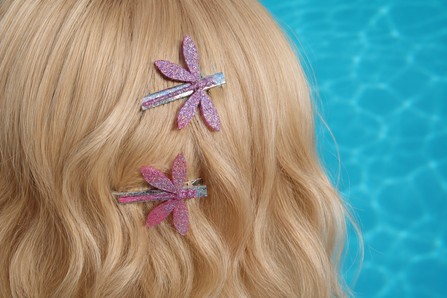 Pink glittery dragonfly hair clips on blonde hair with a pool background