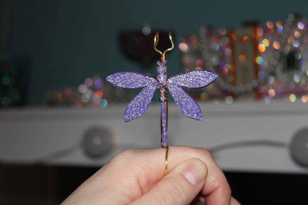 Hand holds a glittery purple dragonfly smoke ring crafted with wire.