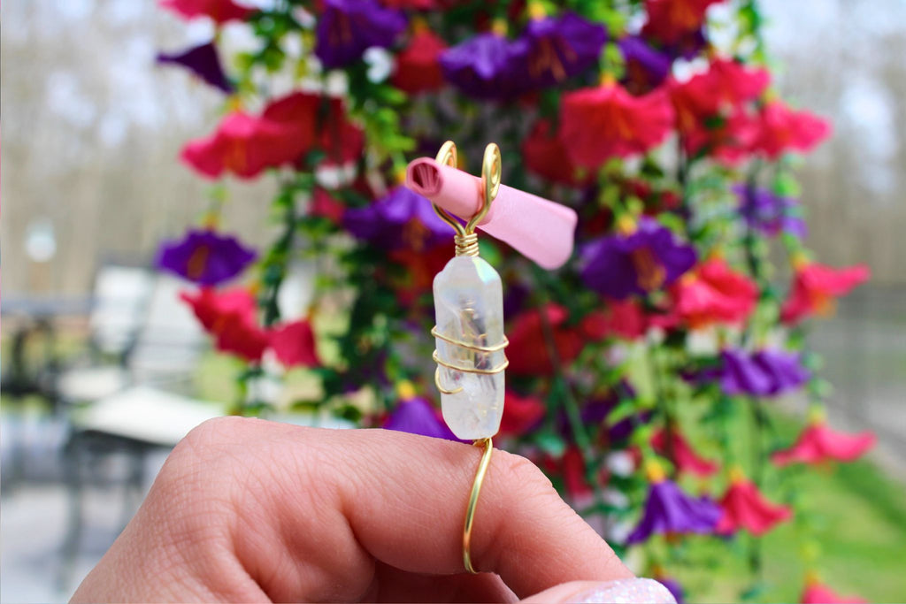 Hand holding a clear quartz crystal wire wrapped smoke ring in front of fake flowers 