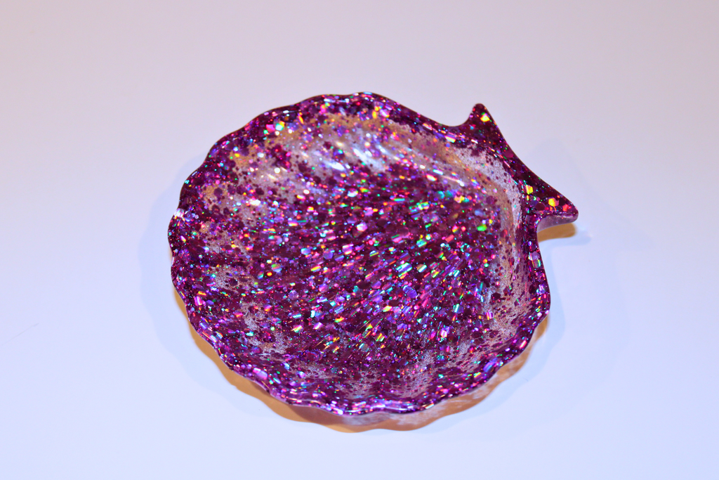 A glittery, purple resin seashell trinket dish sparkles on a white surface.