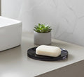 Bar of soap on a black soap dish with a small potted succulent in the background.