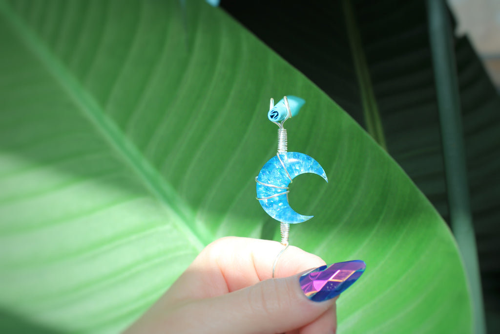 Blue crescent moon smoke ring held against a green leaf background