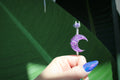 Purple crescent moon smoke ring held by a hand with green leaves in the background