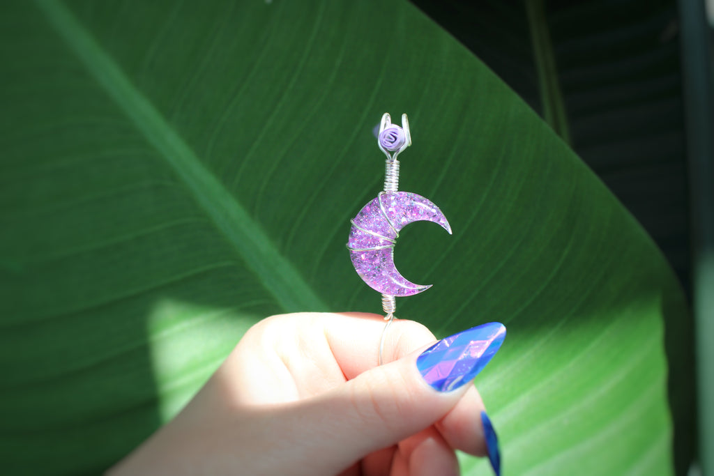 Hand holding a purple crescent moon smoke ring against a green leaf background