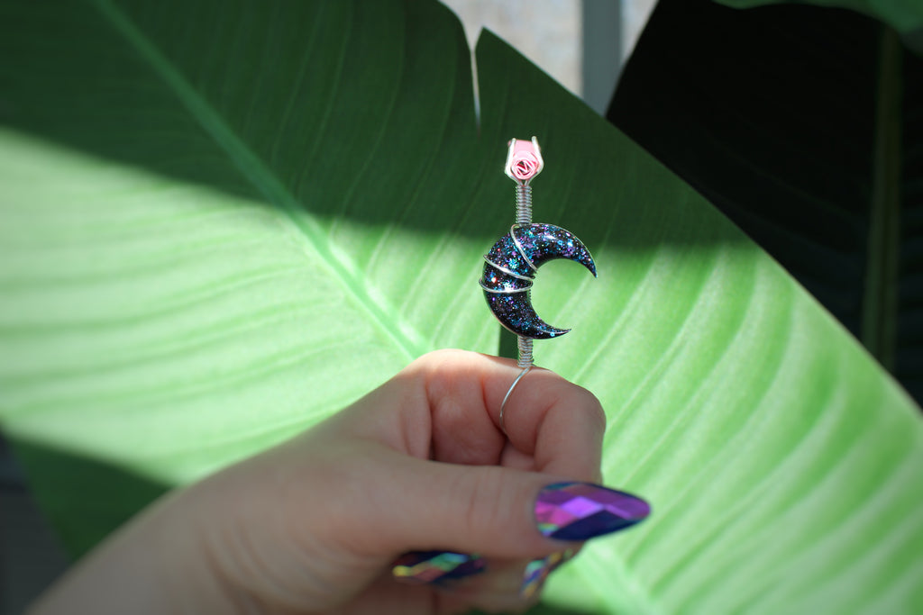 Photo shows a manicured hand holding a galaxy moon smoke ring with a leafy background 