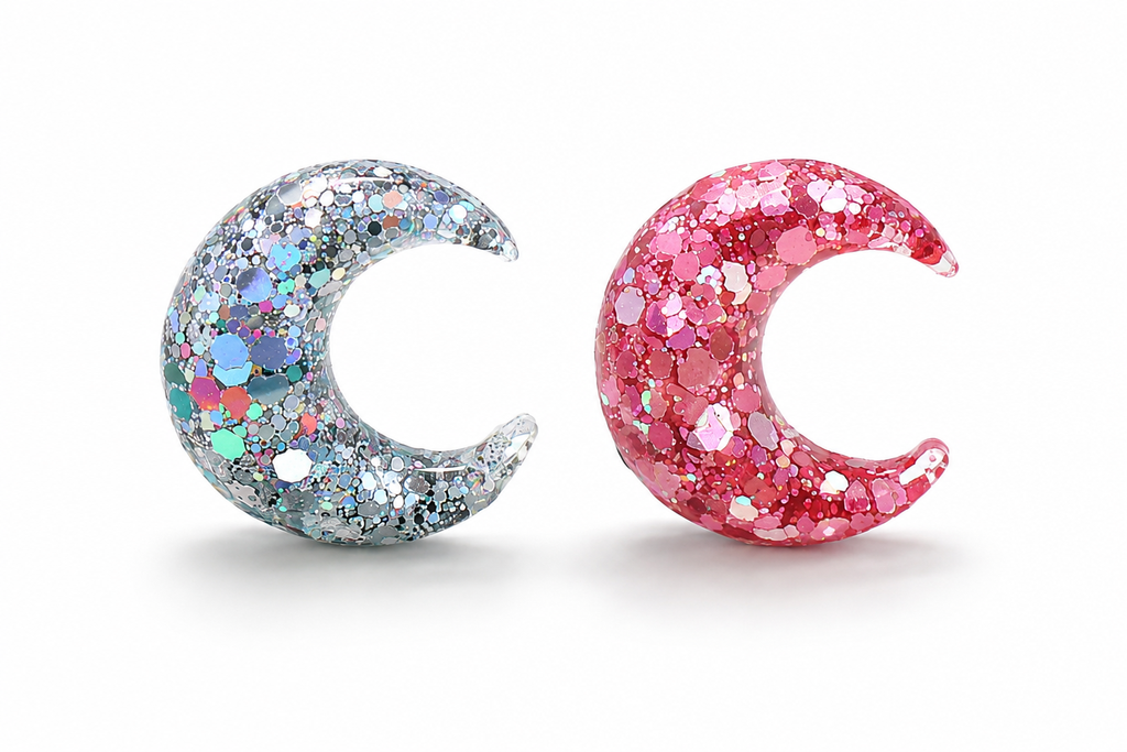 Two glittery moon-shapes, one silver and one pink, on a white background.