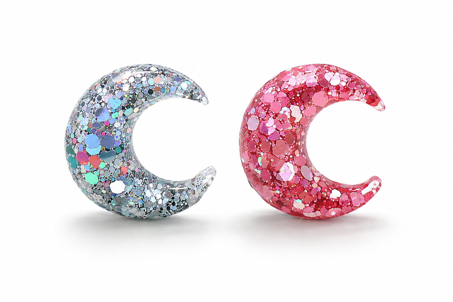 Two glittery moon-shapes, one silver and one pink, on a white background.
