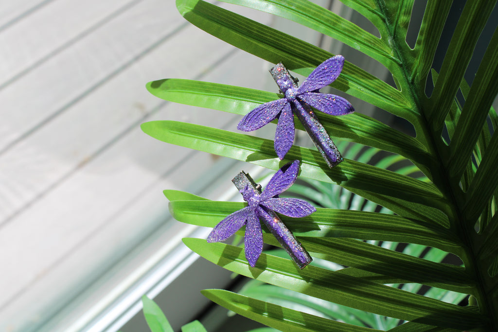 Purple dragonfly hair clips on a green leaf 