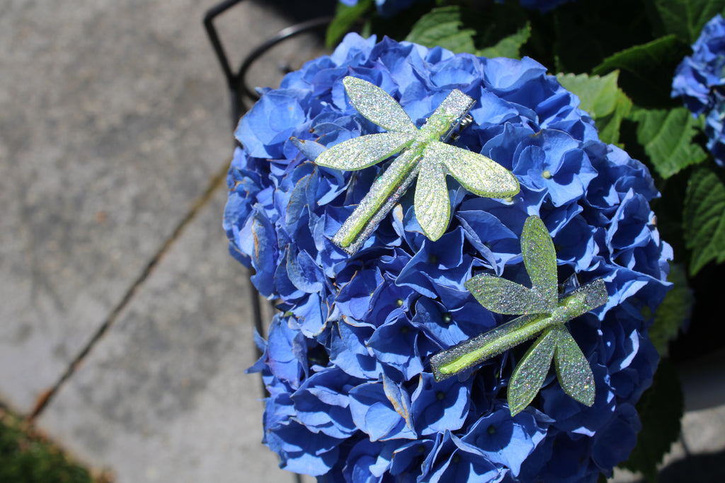 Blue hydrangea flower with green dragonfly-shaped hair clips on a blurred background