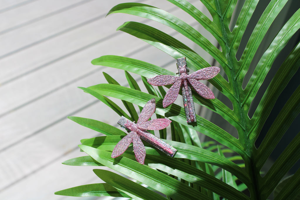 Pink dragonfly hair clips on a green leaf with a white background