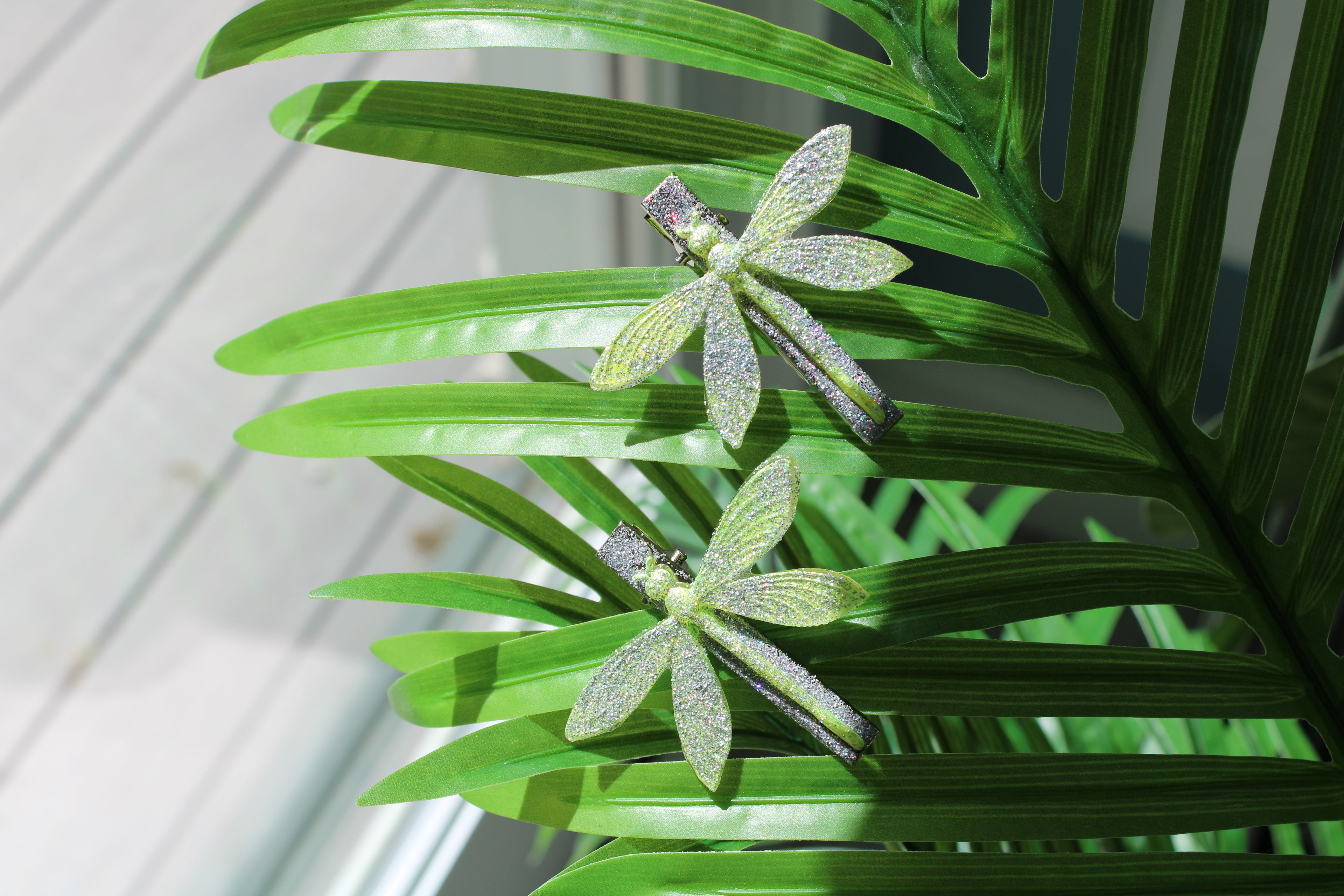 Green dragonfly-shaped hair clips on a leafy background