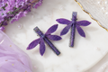 Purple dragonfly hair clips on a marble surface with lavender flowers.