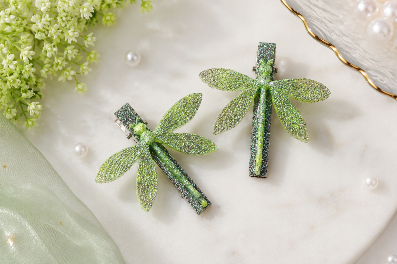 Green dragonfly-shaped hair clips on a marble surface with flowers and pearls.