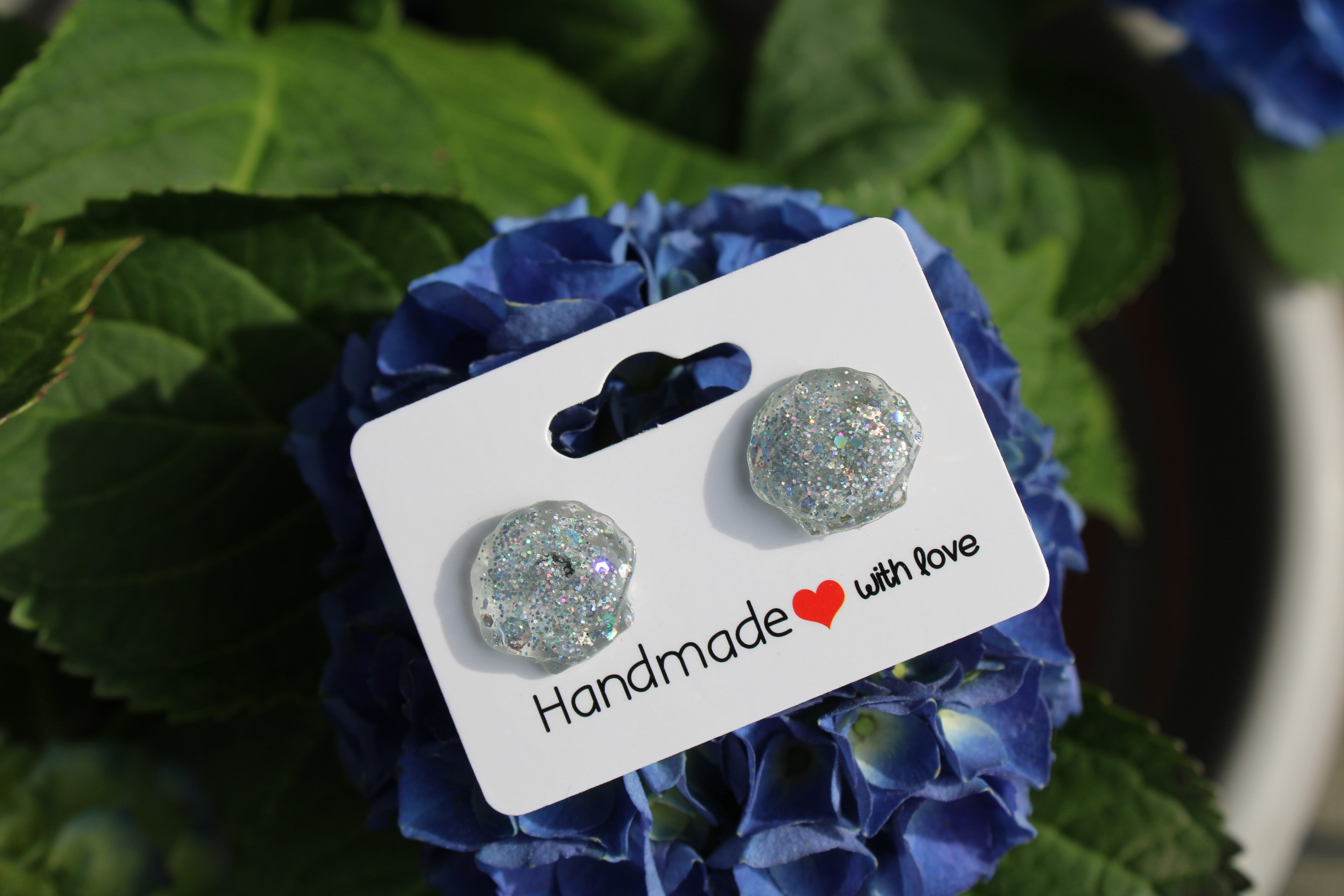 Pair of glittery seashell stud earrings on a 'Handmade with Love' card with blue flowers in the background