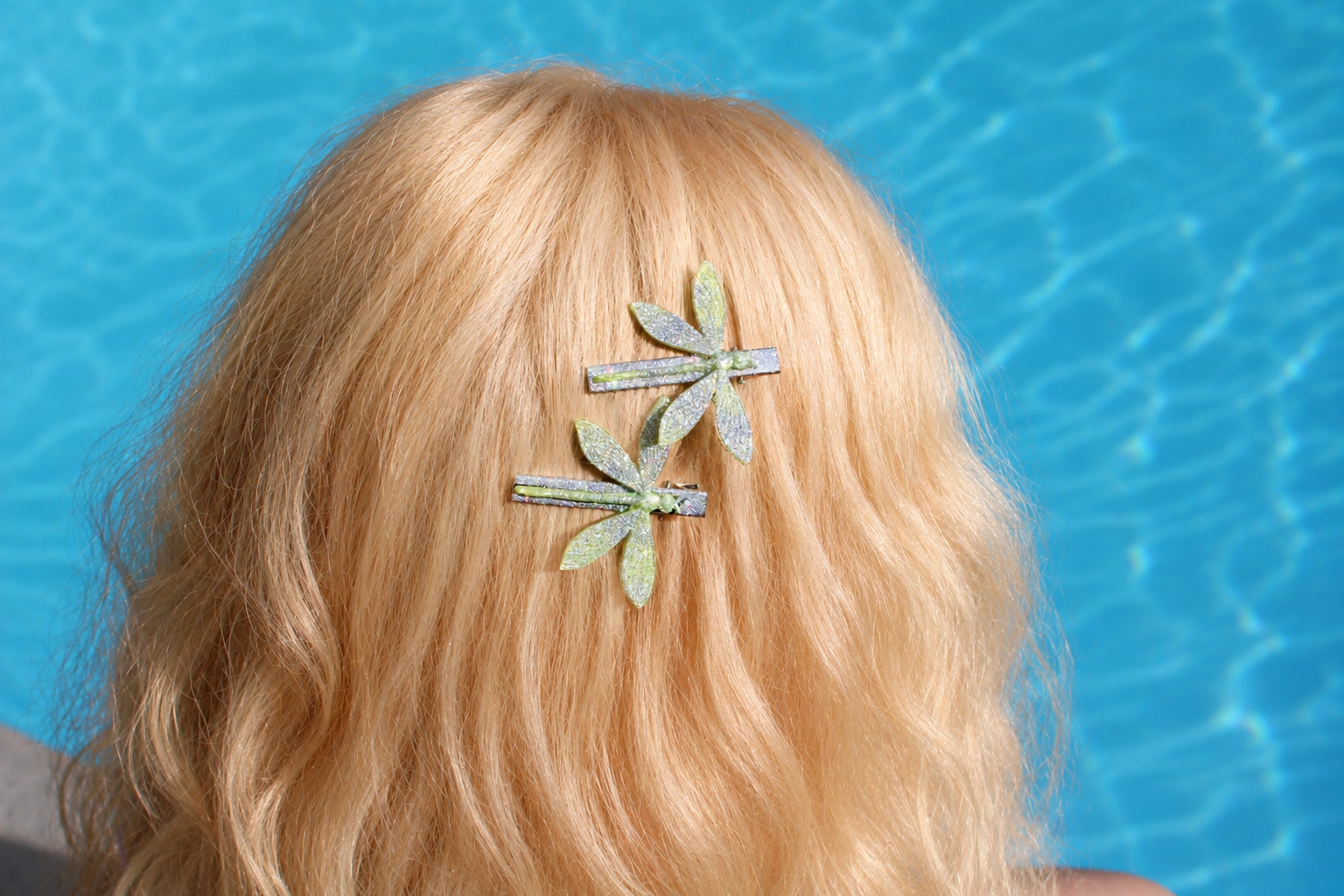 Person with blonde hair wearing a green dragonfly hair clip against a blue water background